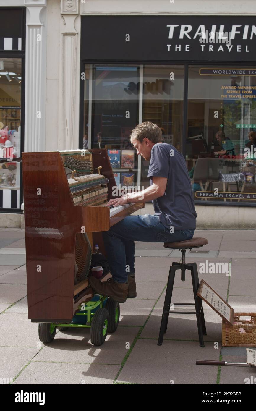 City of Bath High Street Somerset Angleterre Royaume-Uni quartier commercial avec des magasins en arrière-plan Male Busker assis sur un tabouret jouant du piano monté sur roues Banque D'Images