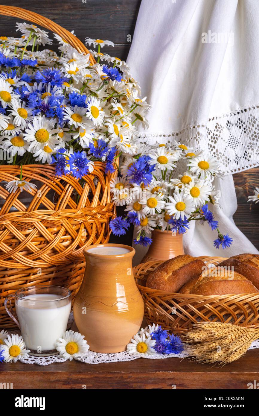 la vie rustique encore. le lait et le pain aux fleurs. les chamomilles et les cornflowers dans un panier Banque D'Images