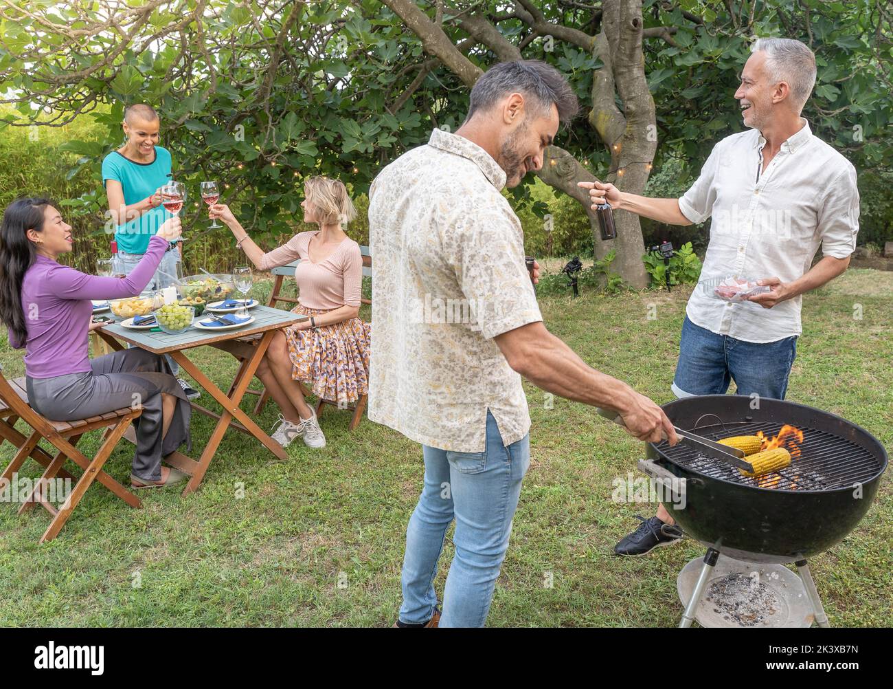 Des amis qui boivent de la bière et cuisent avec le barbecue souriant heureux et riant ensemble dans le patio à l'extérieur. Banque D'Images