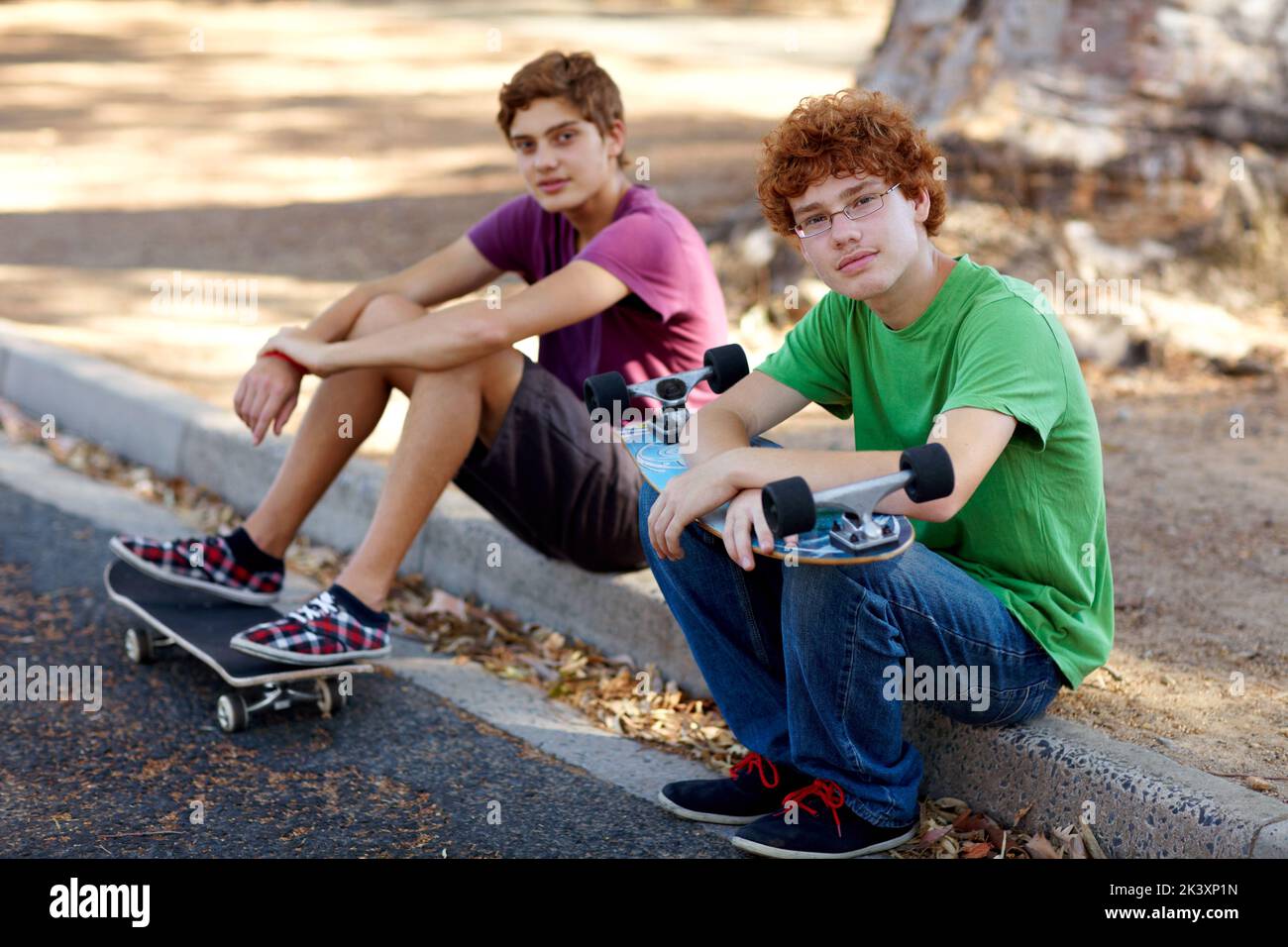 Le week-end, c'est froid. Portrait de deux adolescents assis sur un trottoir avec leurs planches à roulettes. Banque D'Images