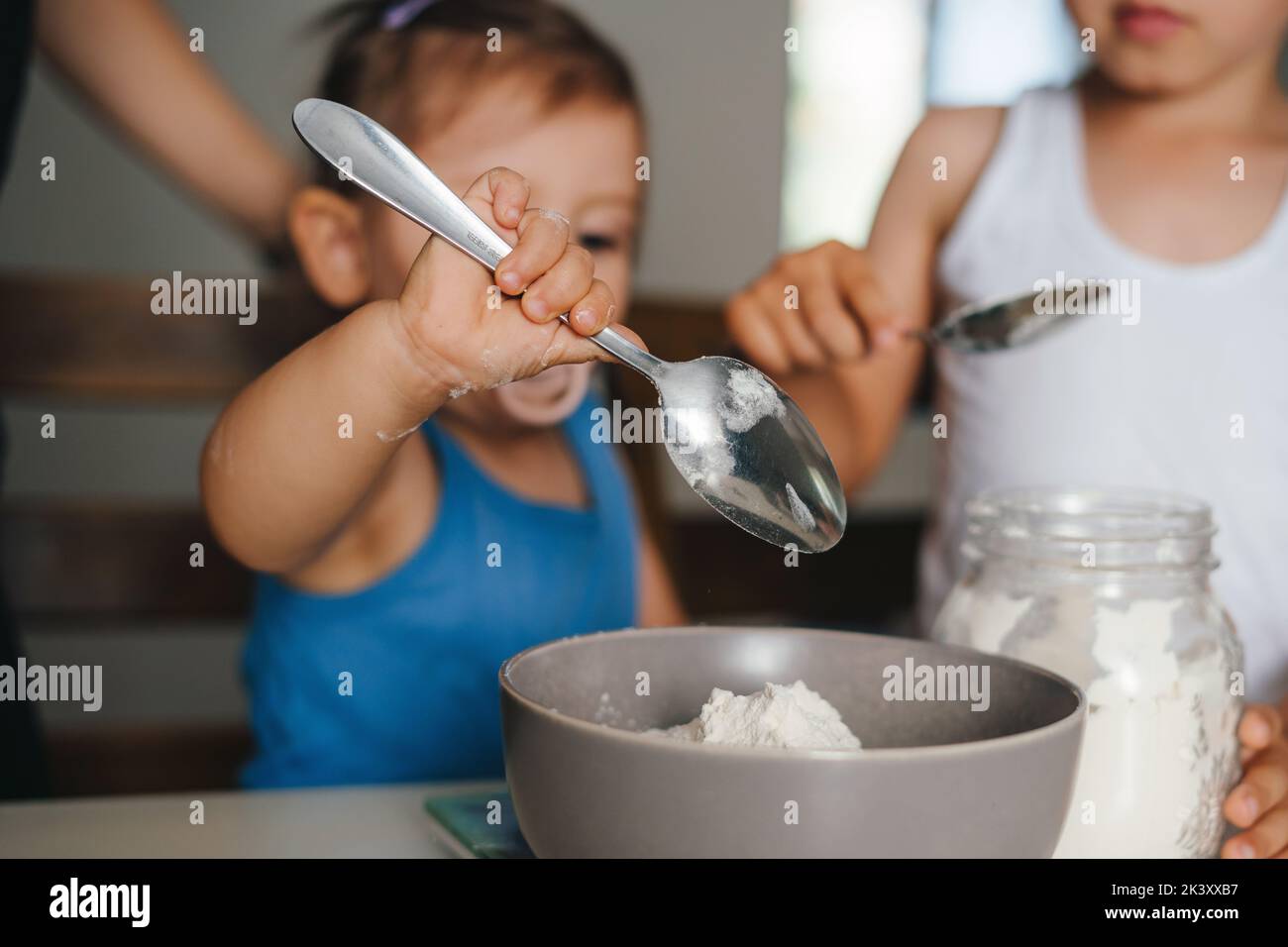 Petite fille mignon ajouter avec une cuillère ingrédients dans le bol tout en faisant la pâte pour la cuisson de la boulangerie dans la cuisine. Préparation de la pâtisserie maison, expression Banque D'Images