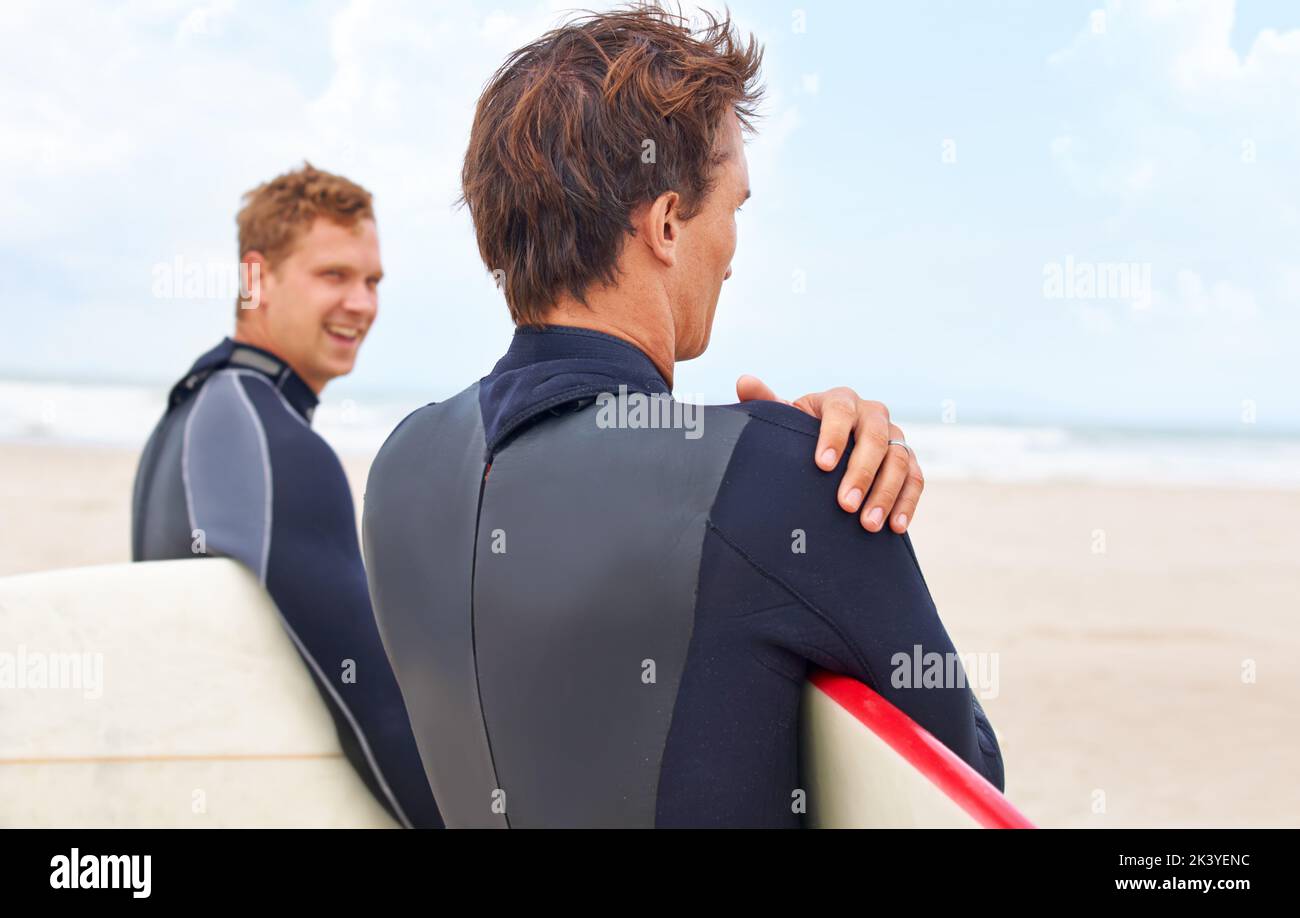 Lié par leur amour du surf. Deux jeunes surfeurs se tenant sur la plage avec l'océan en arrière-plan. Banque D'Images