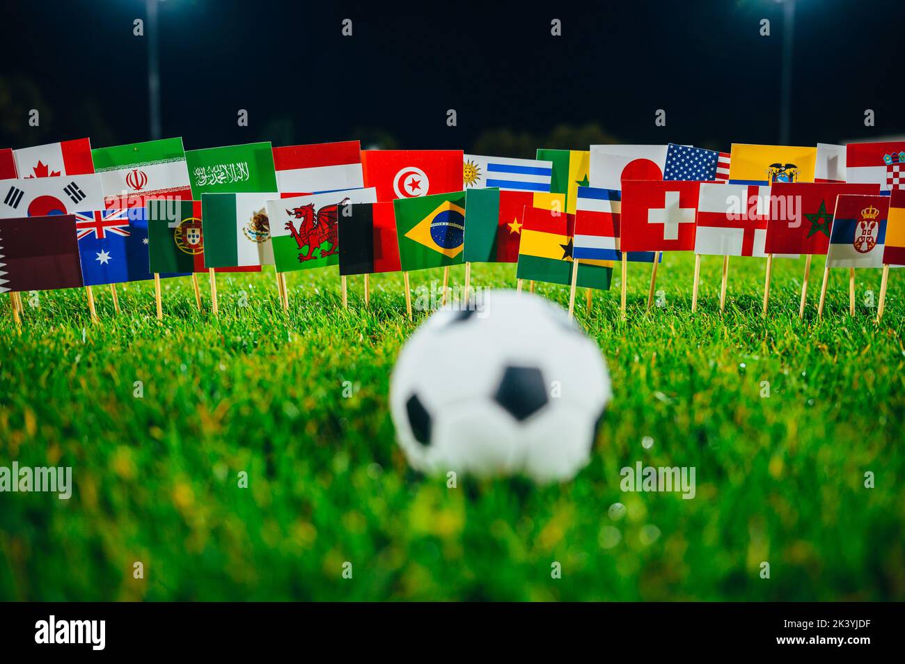 Photo de concept pour le tournoi international de football. Balle sur l'herbe verte et les drapeaux nationaux. Stade de nuit. Arrière-plan noir, espace d'édition. Y compris Banque D'Images