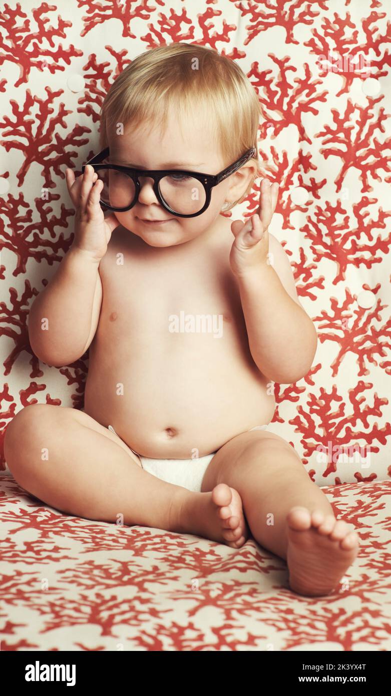 Quel curieux petit gars. Un adorable bébé garçon assis dans une neppy et jouant avec une paire de lunettes. Banque D'Images