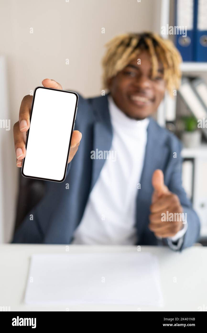 Comme un geste. Homme noir de bureau. Application mobile. Joyeux homme de beau défoqué montrant smartphone vide écran de soutien geste dans la pièce lumineuse Banque D'Images Comme un geste. Homme noir de bureau. Application mobile. Joyeux homme de beau défoqué montrant smartphone vide écran de soutien geste dans la pièce lumineuse Banque D'Images