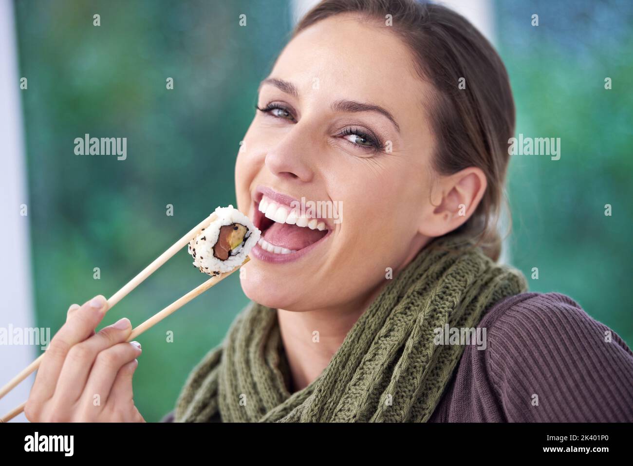 C'est comme ça que je roule. Une jeune femme souriant tout en tenant un morceau de sushi. Banque D'Images