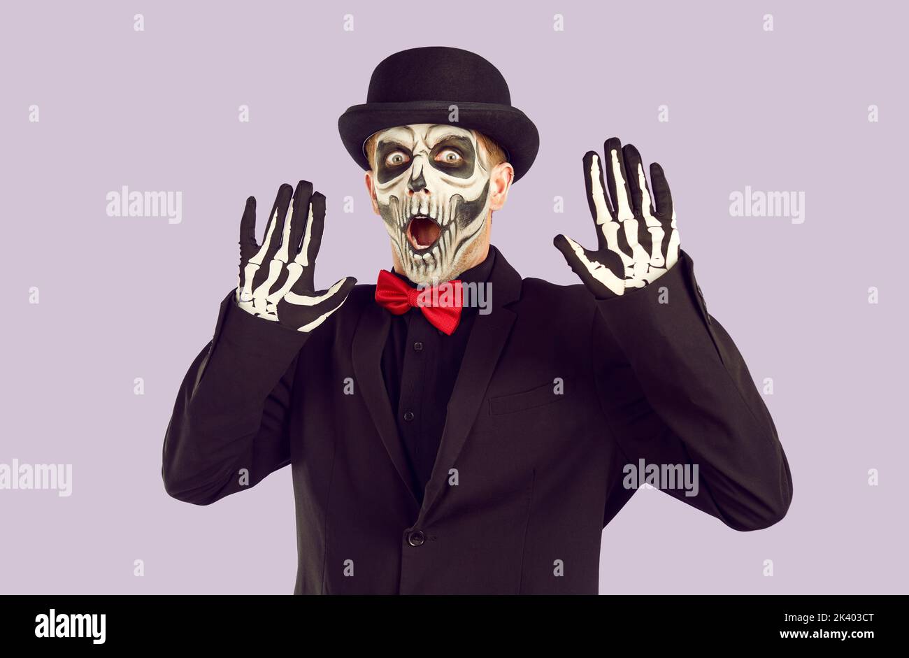 Jeune homme avec le maquillage squelette et dans la tenue d'Halloween élégante lève ses mains avec peur. Banque D'Images