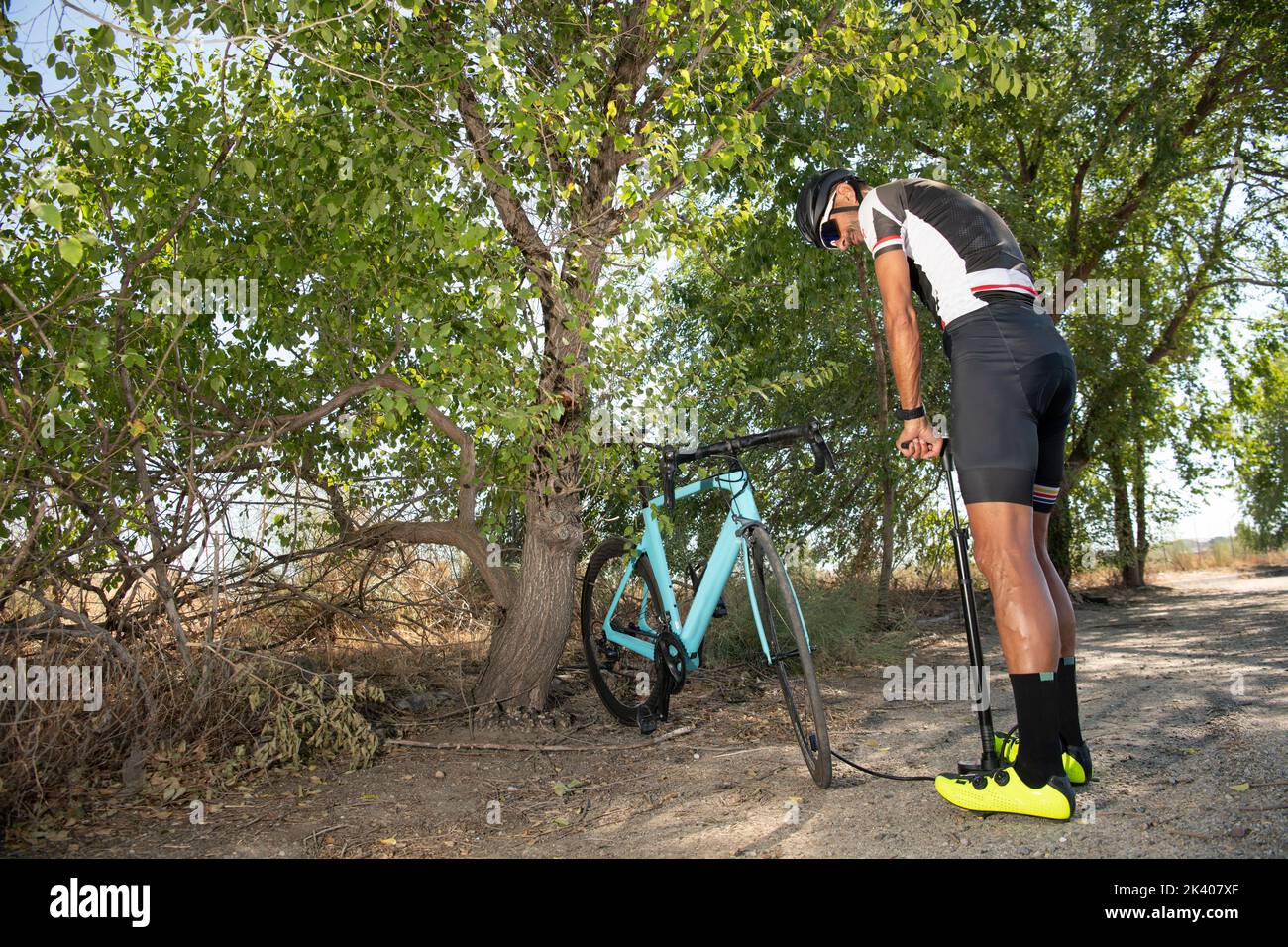 Un cycliste répare un vélo sur une route forestière par temps ensoleillé Banque D'Images