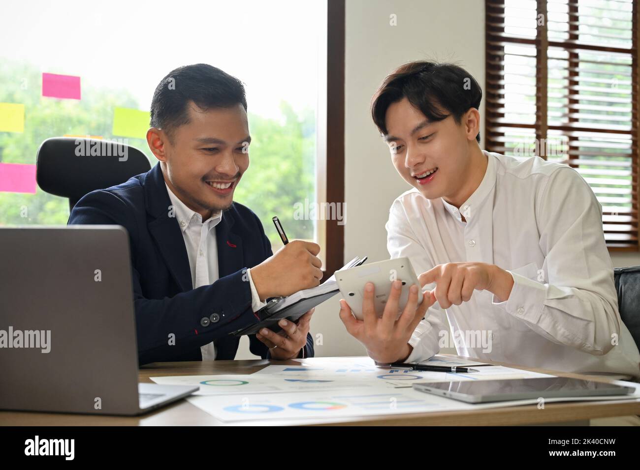 Beau et joyeux jeune homme d'affaires ou employé d'Asie ayant une belle conversation avec son collègue pendant le travail ensemble. Banque D'Images