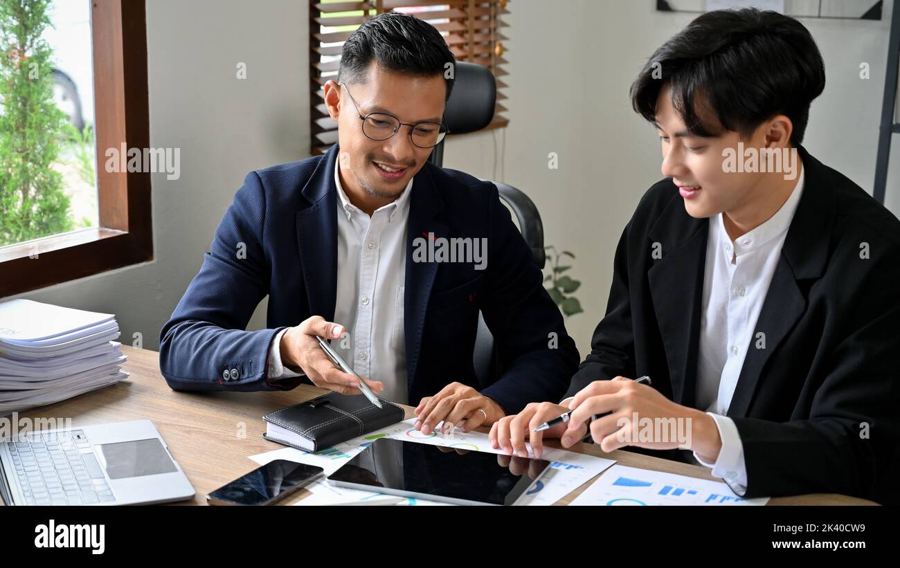 Homme d'affaires asiatique élégant et professionnel, offrant des conseils et expliquant quelque chose à son personnel masculin tout en travaillant ensemble au bureau. Banque D'Images