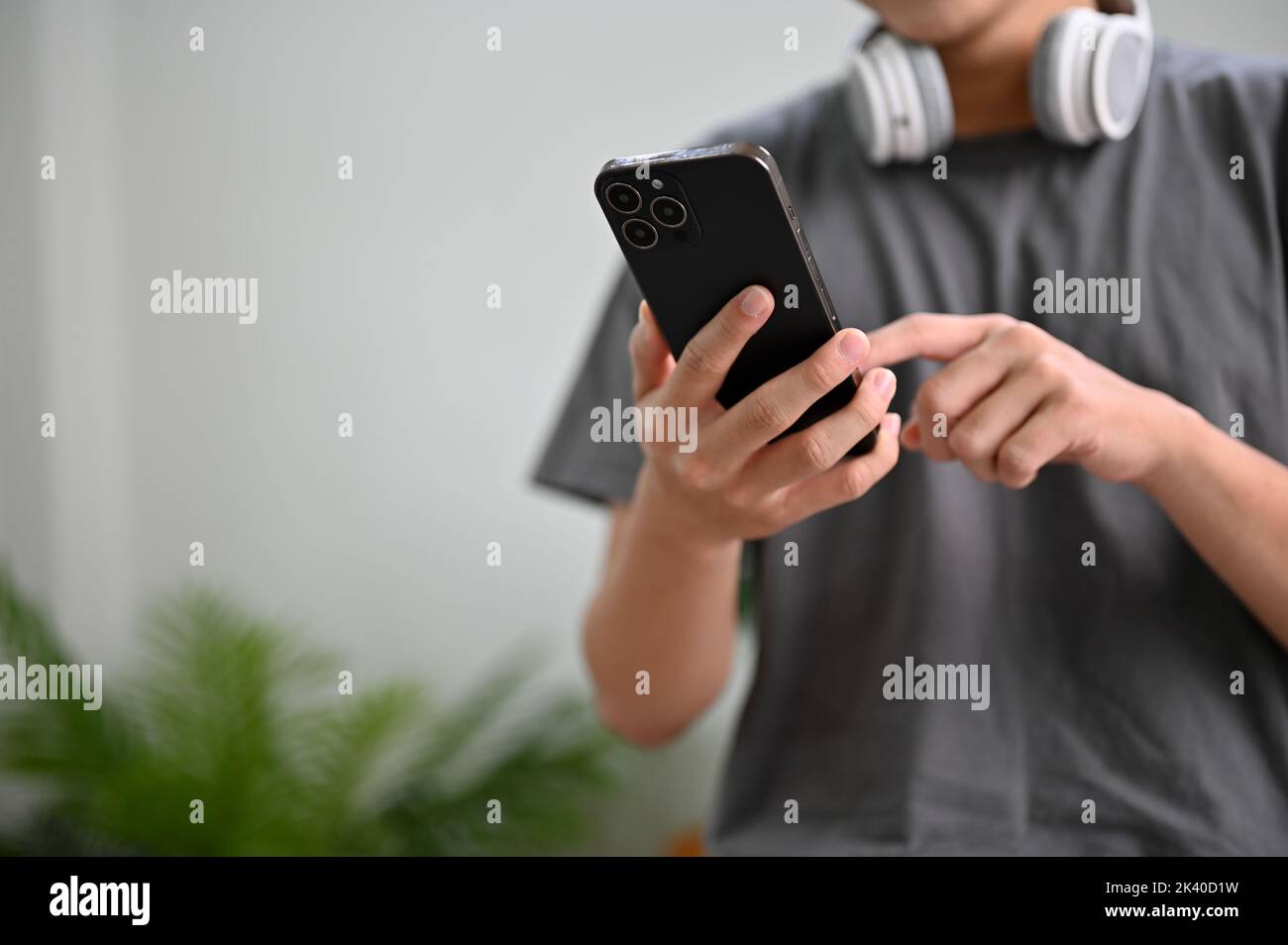 Jeune homme asiatique vêque dans un salon, utilisant un smartphone pour envoyer des messages à ses amis, tester une nouvelle application, commander des aliments de livraison sur le Banque D'Images