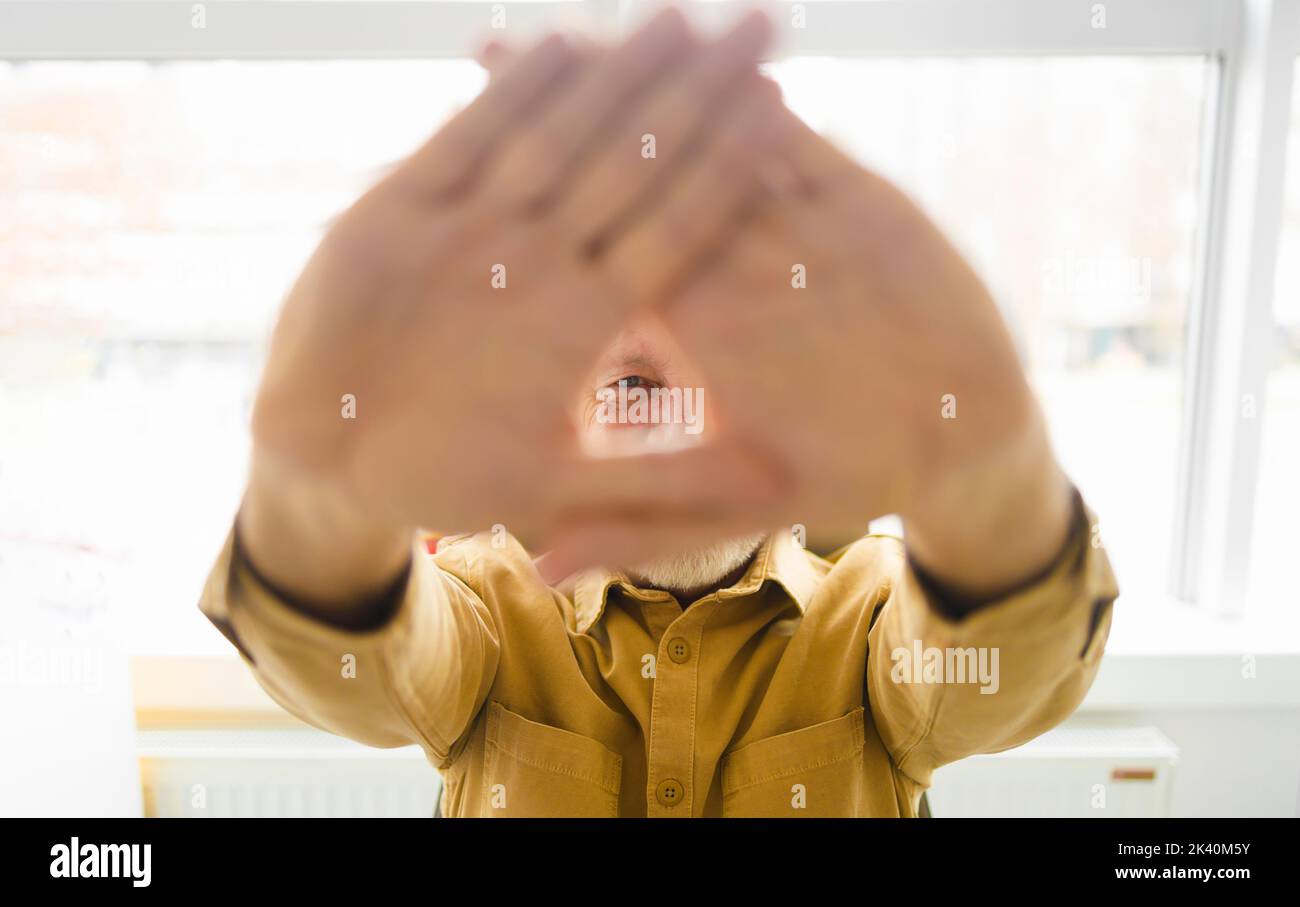 Homme âgé montrant ses mains et faisant un exercice oculaire Banque D'Images
