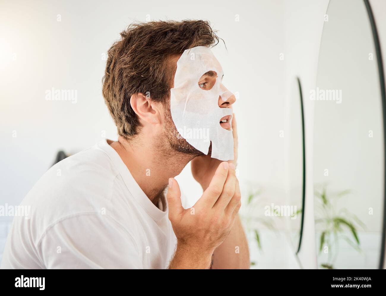 Homme, miroir de salle de bains et soin de la peau masque beauté cosmétiques nettoyant pour problèmes d'huile ou traitement d'hygiène. Jeune homme touchante, hydratant Banque D'Images