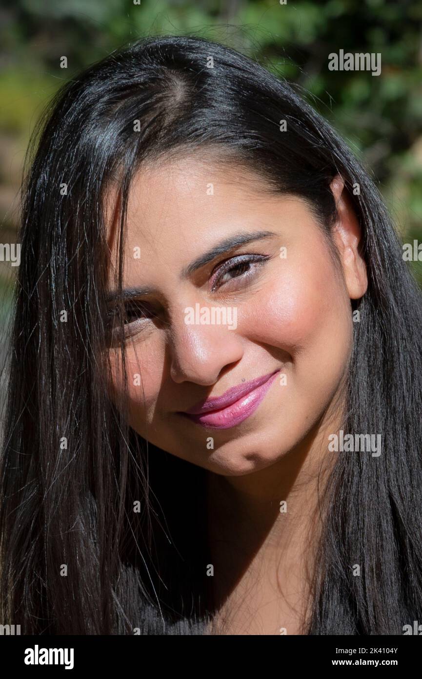 Belle jeune femme avec de longs cheveux foncés, les yeux sombres et le menton fendu, souriant vers la caméra Banque D'Images