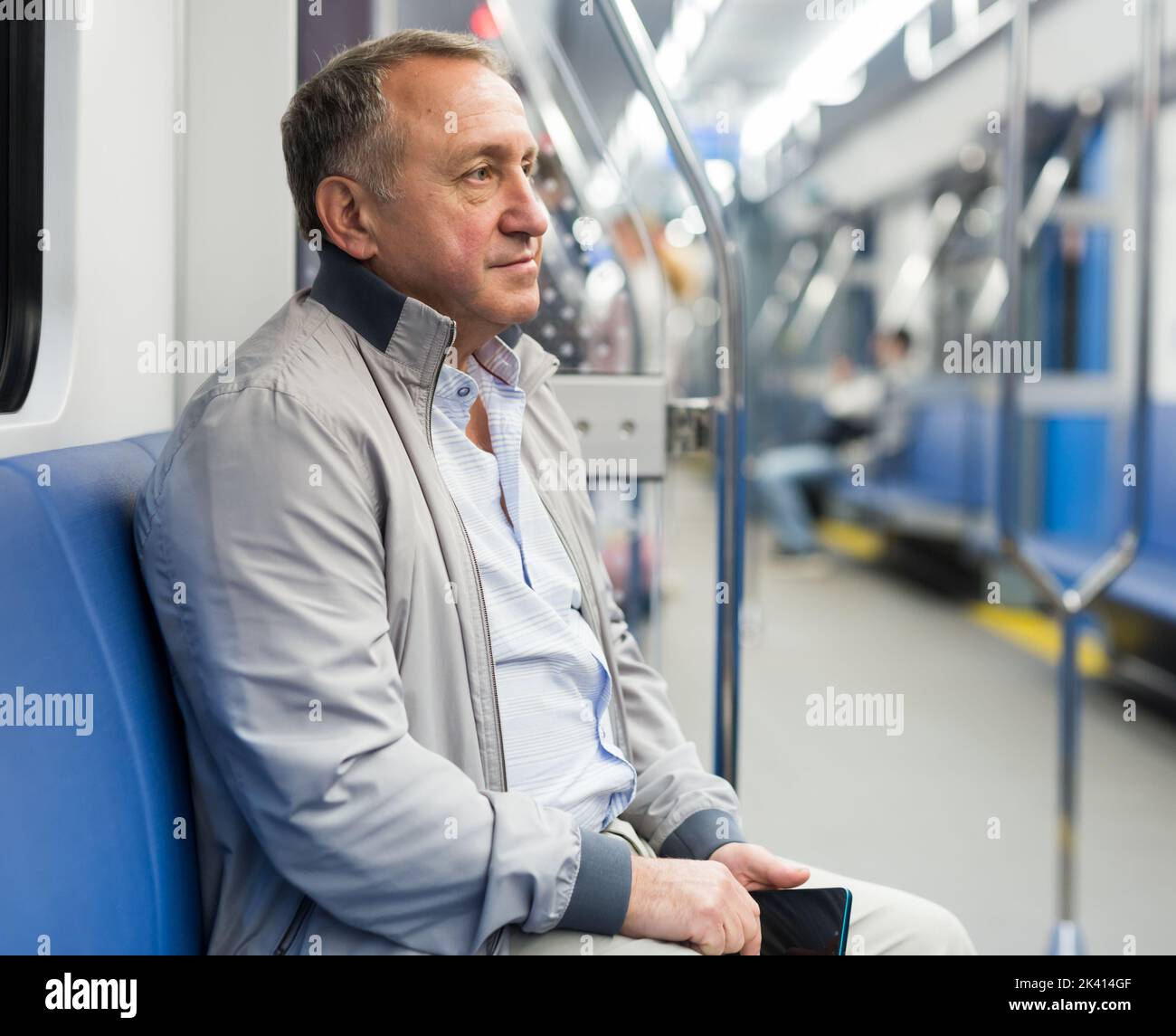 Homme âgé positif assis dans une voiture de métro vide pendant que le train est en mouvement Banque D'Images