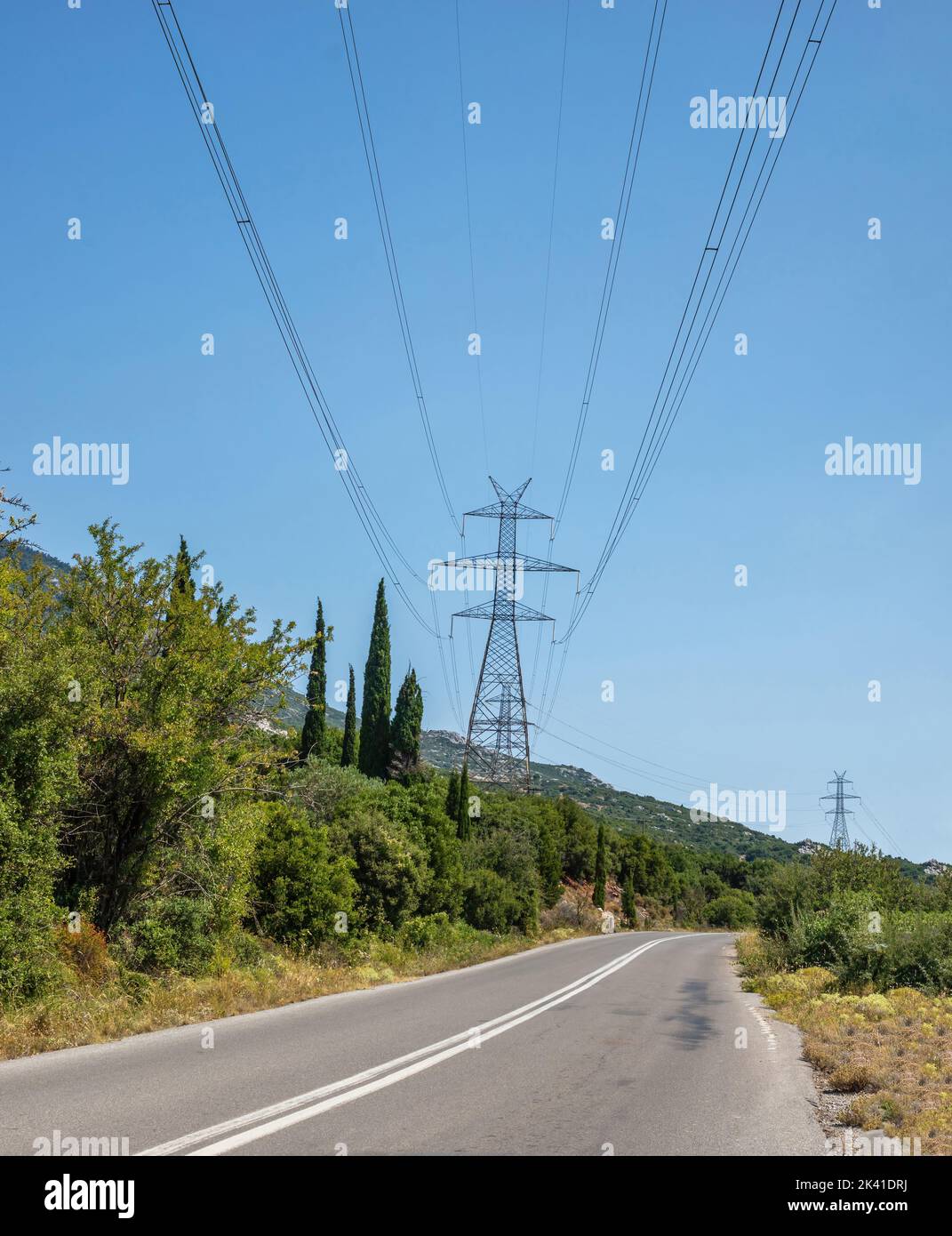 Lignes haute tension et pylônes sur une route asphaltée, fond bleu ciel. Pôle métallique, transmission d'énergie électrique Banque D'Images