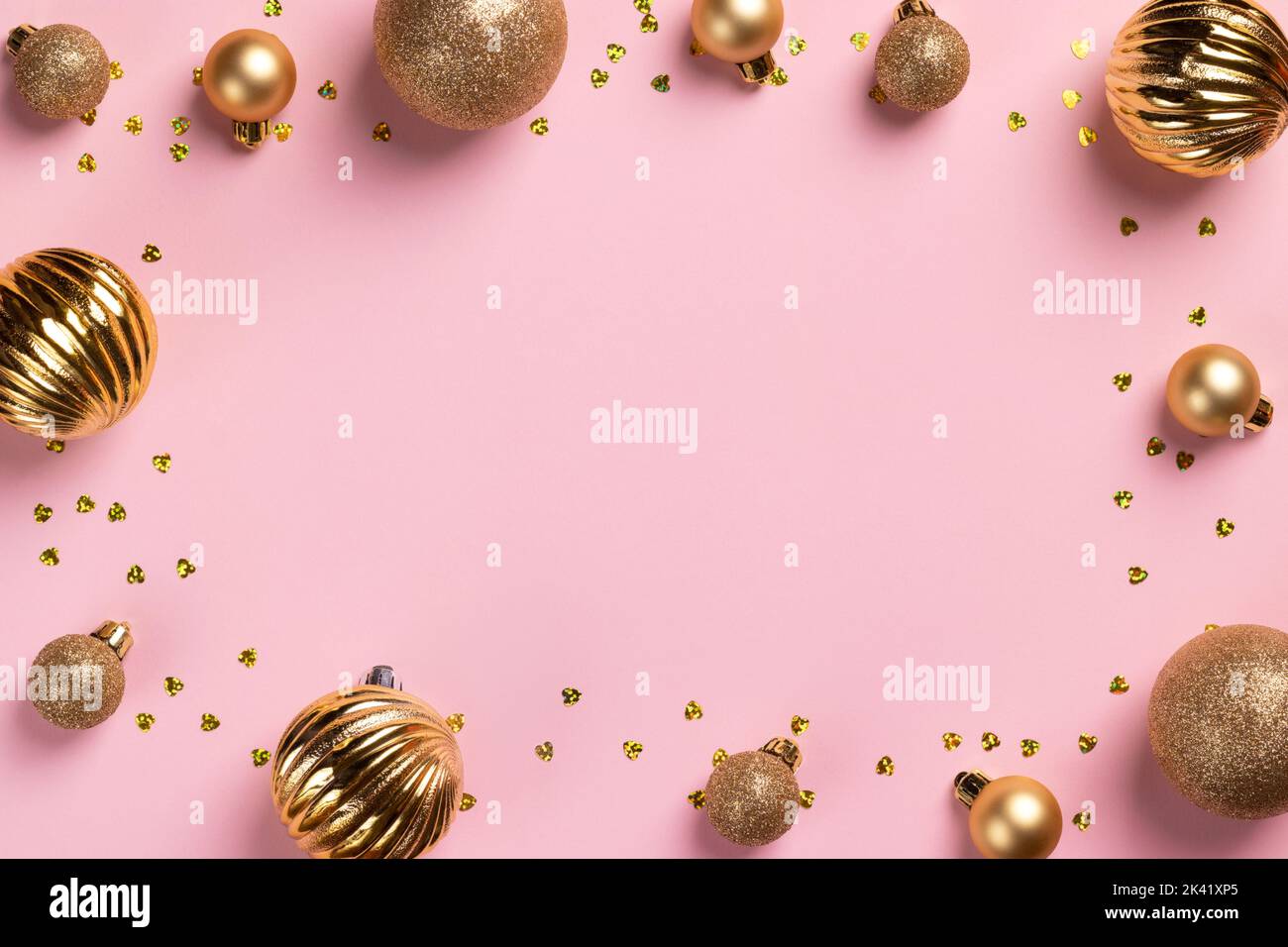 Cadre pour cartes de Noël avec boules dorées à paillettes et confetti sur fond rose avec espace pour les copies Banque D'Images