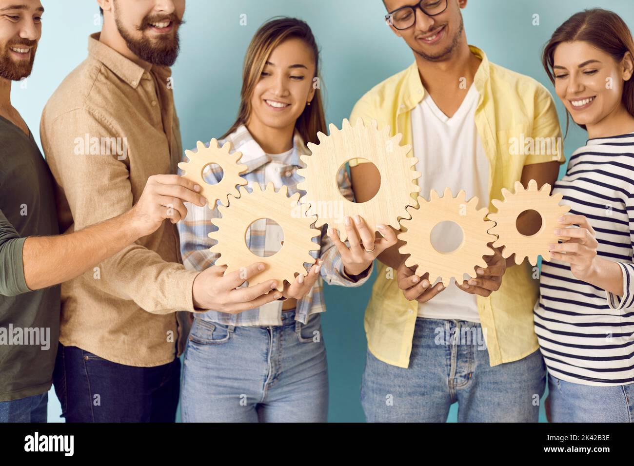 Une équipe multiraciale de jeunes heureux qui relient les roues dentées comme symbole du travail d'équipe Banque D'Images