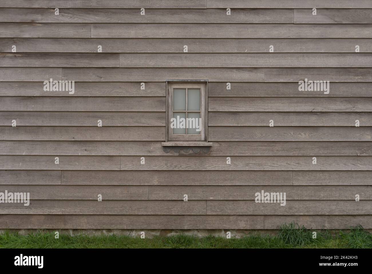 Texture de placage en bois rustique avec petite fenêtre en bois centrée, fond horizontal non peint de vieux bois, herbe et plantes à la base Banque D'Images