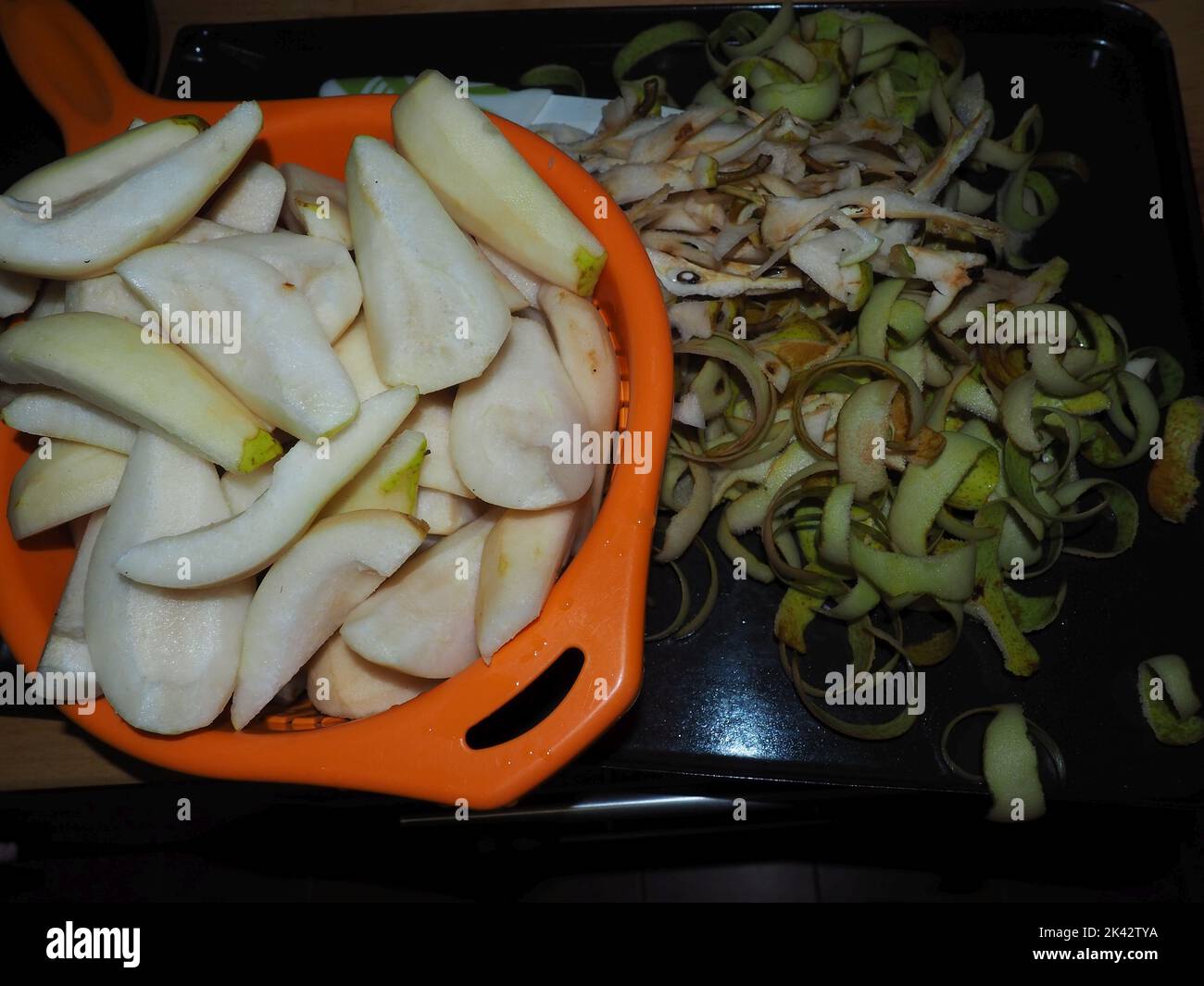 processus de préservation de la poire. Pelures de poire placées sur un essai de métal avec un bol d'orange plein de fruits de poire nettoyés et coupés. Banque D'Images