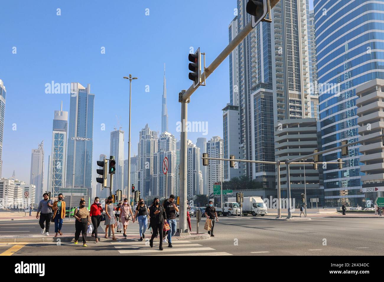 Eau, Dubaï - 27 novembre 2021 : les gens marchent le long de la traversée piétonne dans le centre d'affaires de Dubaï. Les hommes en costume et les masques médicaux se précipitent pour travailler sur fond d'énormes gratte-ciel. Photo de haute qualité Banque D'Images