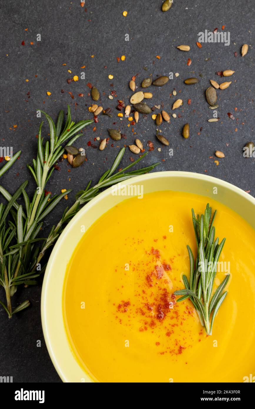 Image verticale d'un bol de soupe de carottes avec garniture au romarin, et graines sur ardoise, copier l'espace Banque D'Images