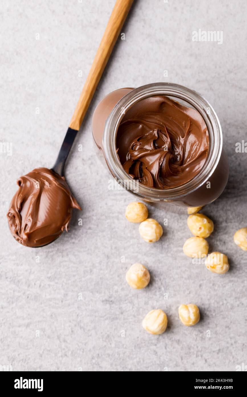 Image verticale de la cuillère avec la crème au chocolat, le pot et les noix sur la surface grise Banque D'Images