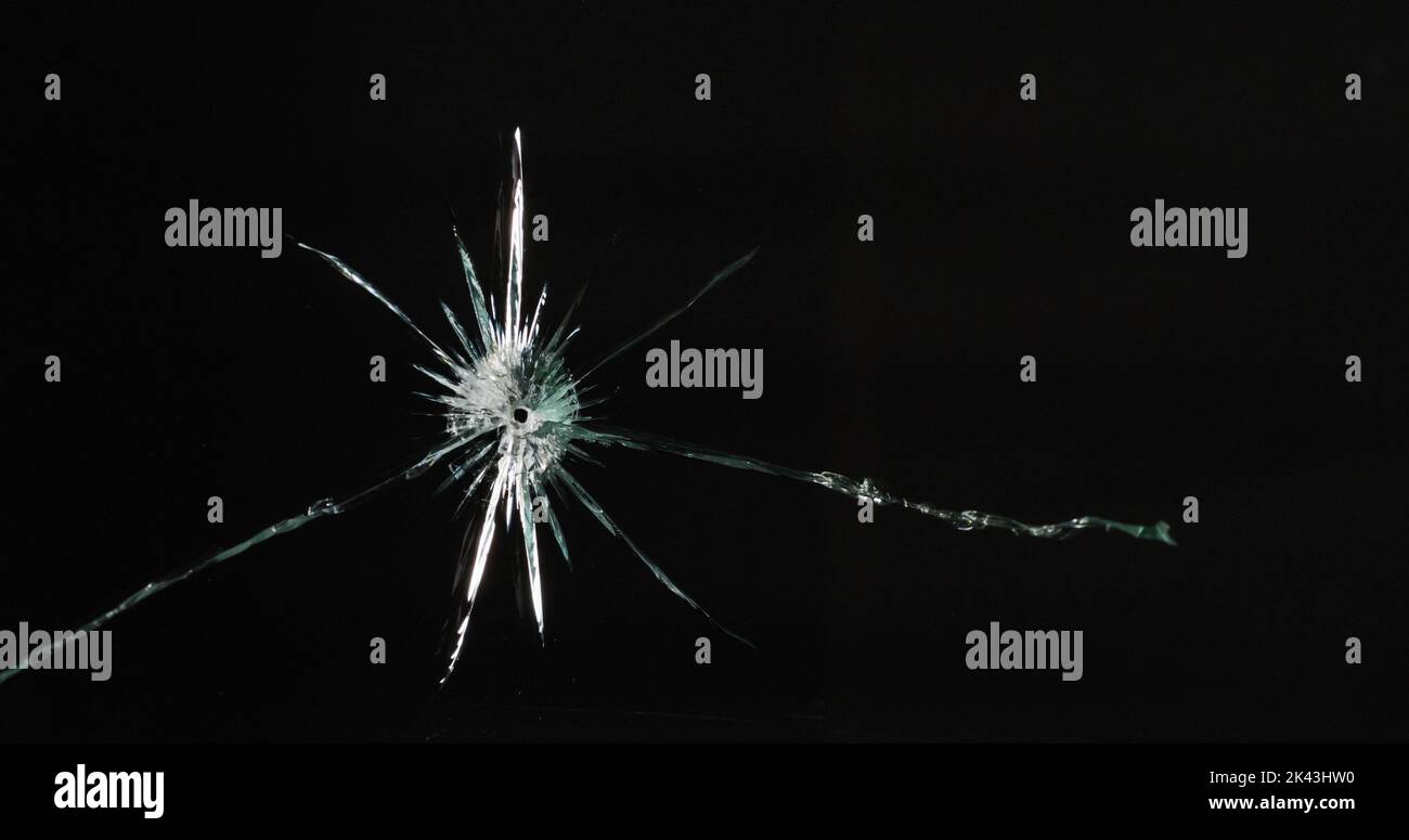 Gros plan d'un panneau de verre cassé et fissuré avec trou rond, sur fond noir avec espace de copie Banque D'Images