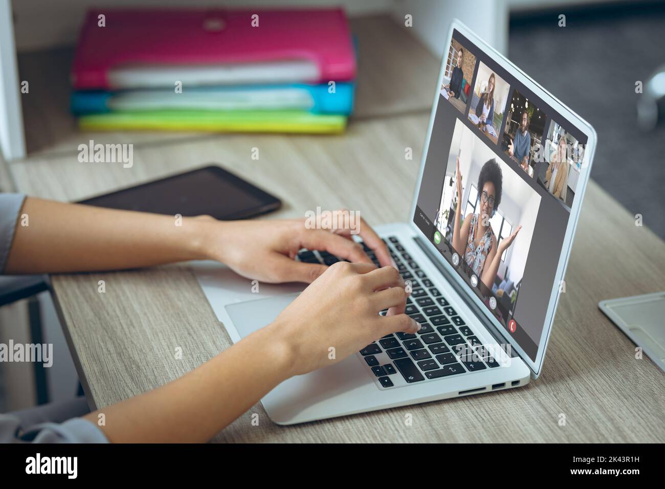 Les mains rognées d'une femme caucasienne se nouent au clavier tout en discutant avec des collègues au-dessus d'un ordinateur portable Banque D'Images