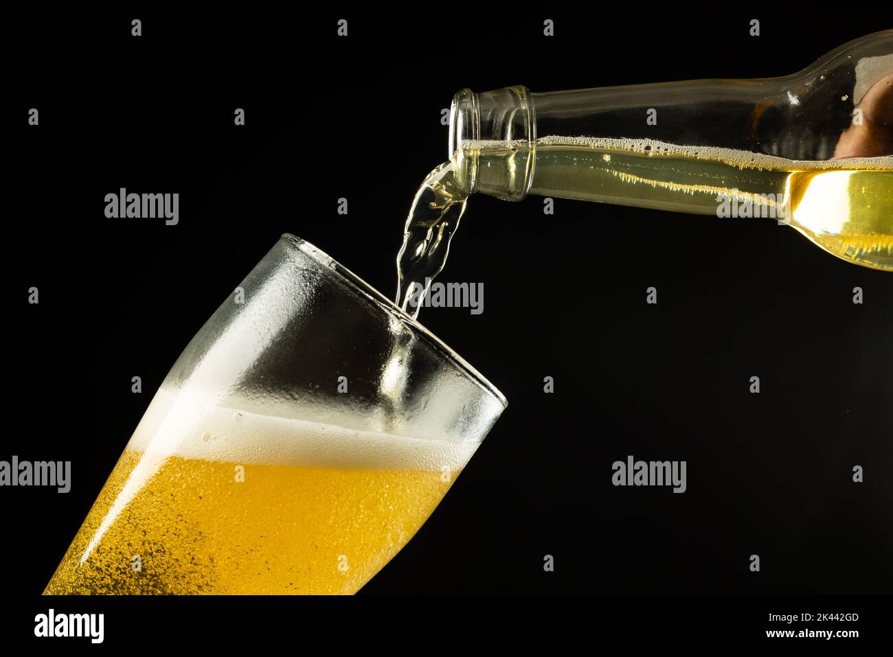 Image horizontale d'une bouteille transparente de bière lager qui coule dans le verre sur fond noir, avec espace de copie Banque D'Images