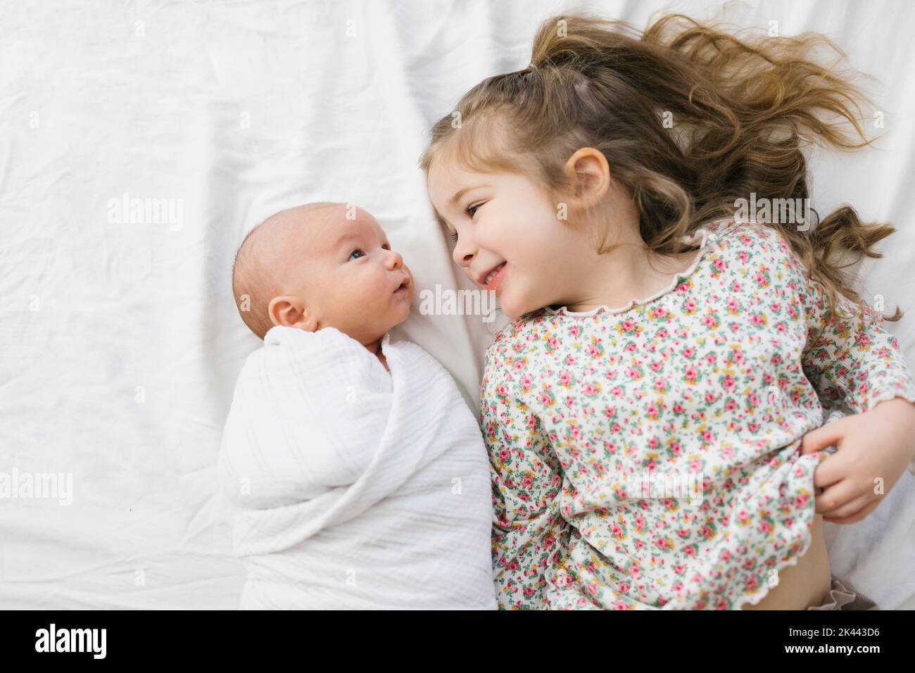 Vue de dessus de fille (2-3) souriant à bébé frère (0-1 mois) sur le lit Banque D'Images