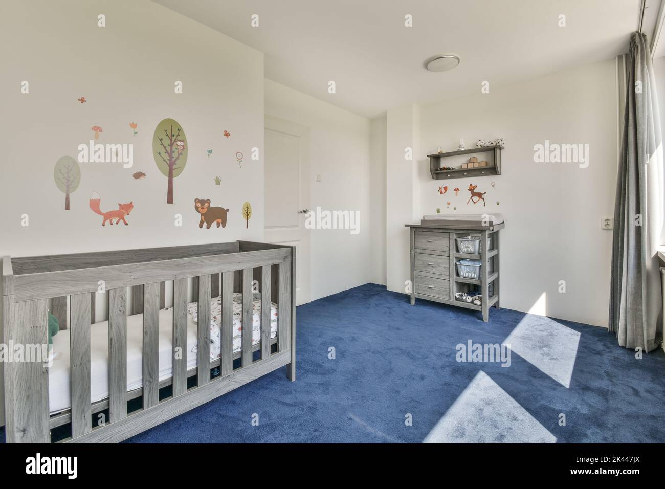 Intérieur de la chambre blanche avec lit bébé gris et près de la fenêtre avec commode grise dans la lumière du jour Banque D'Images