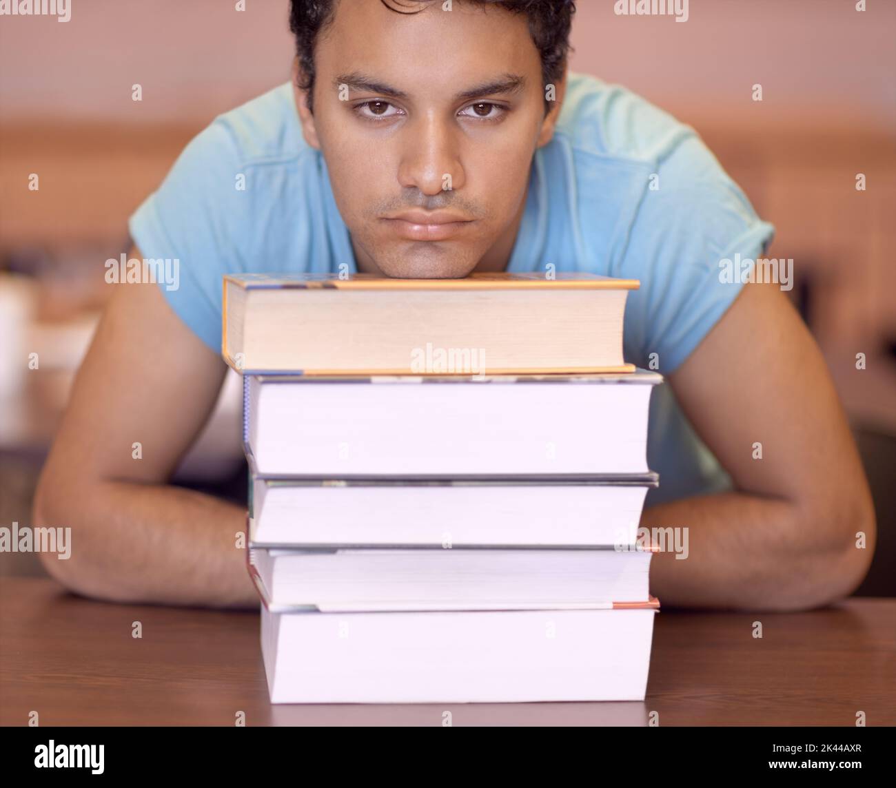 Tellement à étudier. Portrait d'un jeune homme qui a l'air s'ennuyer tout en se reposant la tête sur certains manuels scolaires. Banque D'Images