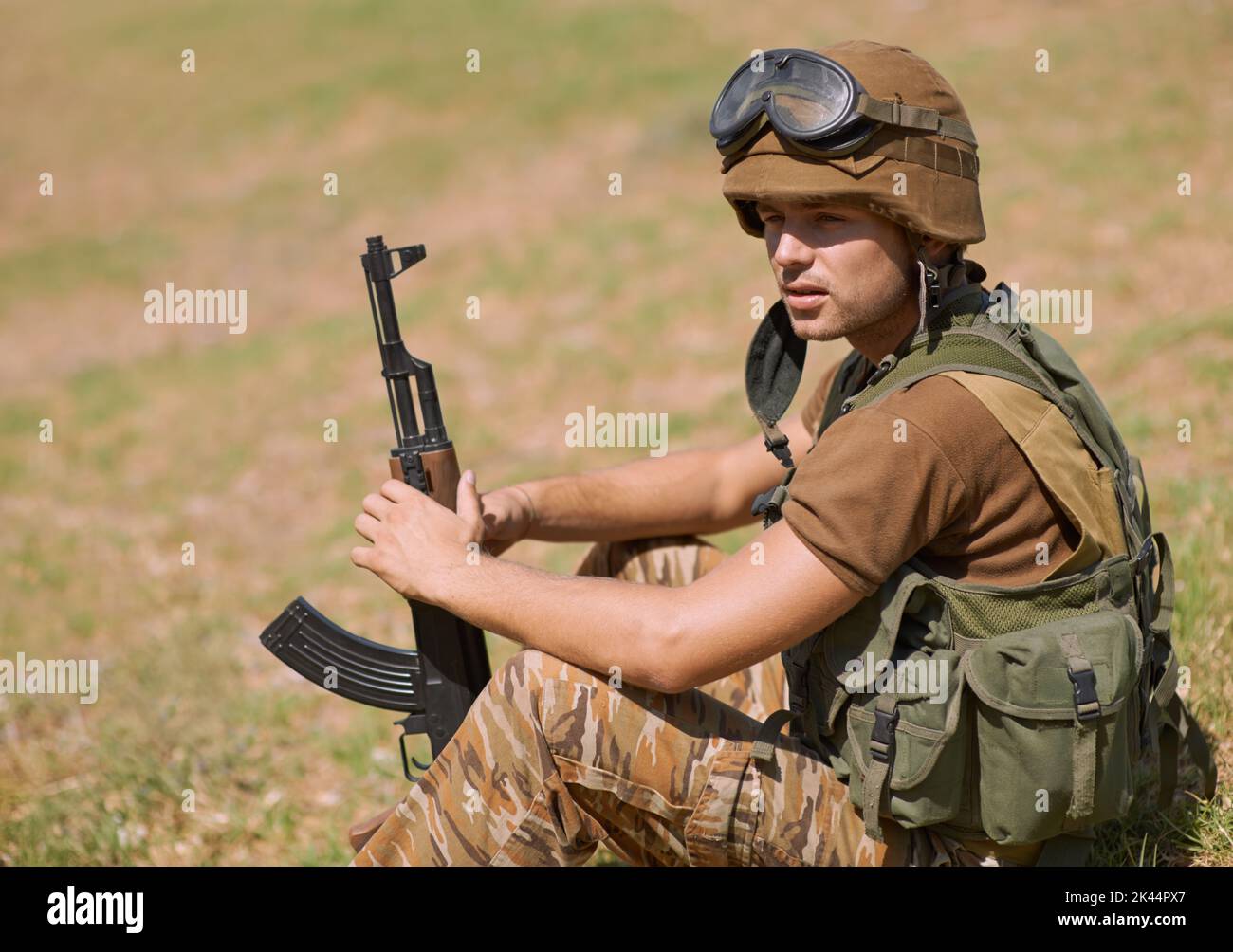 En attendant l'ennemi. Un jeune soldat assis sur l'herbe à l'extérieur. Banque D'Images