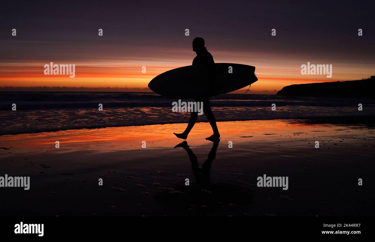 Un surfeur entre dans l'eau à la plage de Tynemouth Longsands avant le lever du soleil. Date de la photo: Vendredi 30 septembre 2022. Banque D'Images
