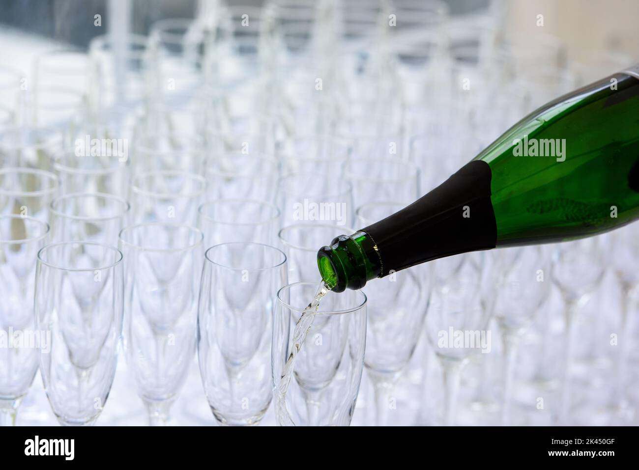 gros plan d'une bouteille de champagne pooring du champagne dans une flûte de champagne contre des verres flous en arrière-plan Banque D'Images