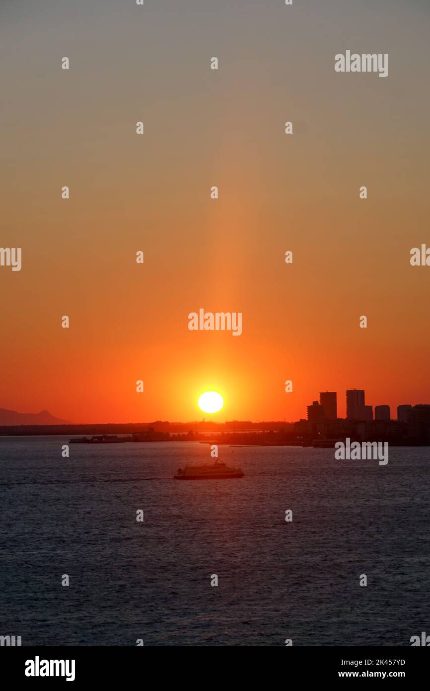 Le soleil lumineux au coucher du soleil rouge sur la mer Égée à Izmir, Turquie avec des bâtiments en arrière-plan Banque D'Images