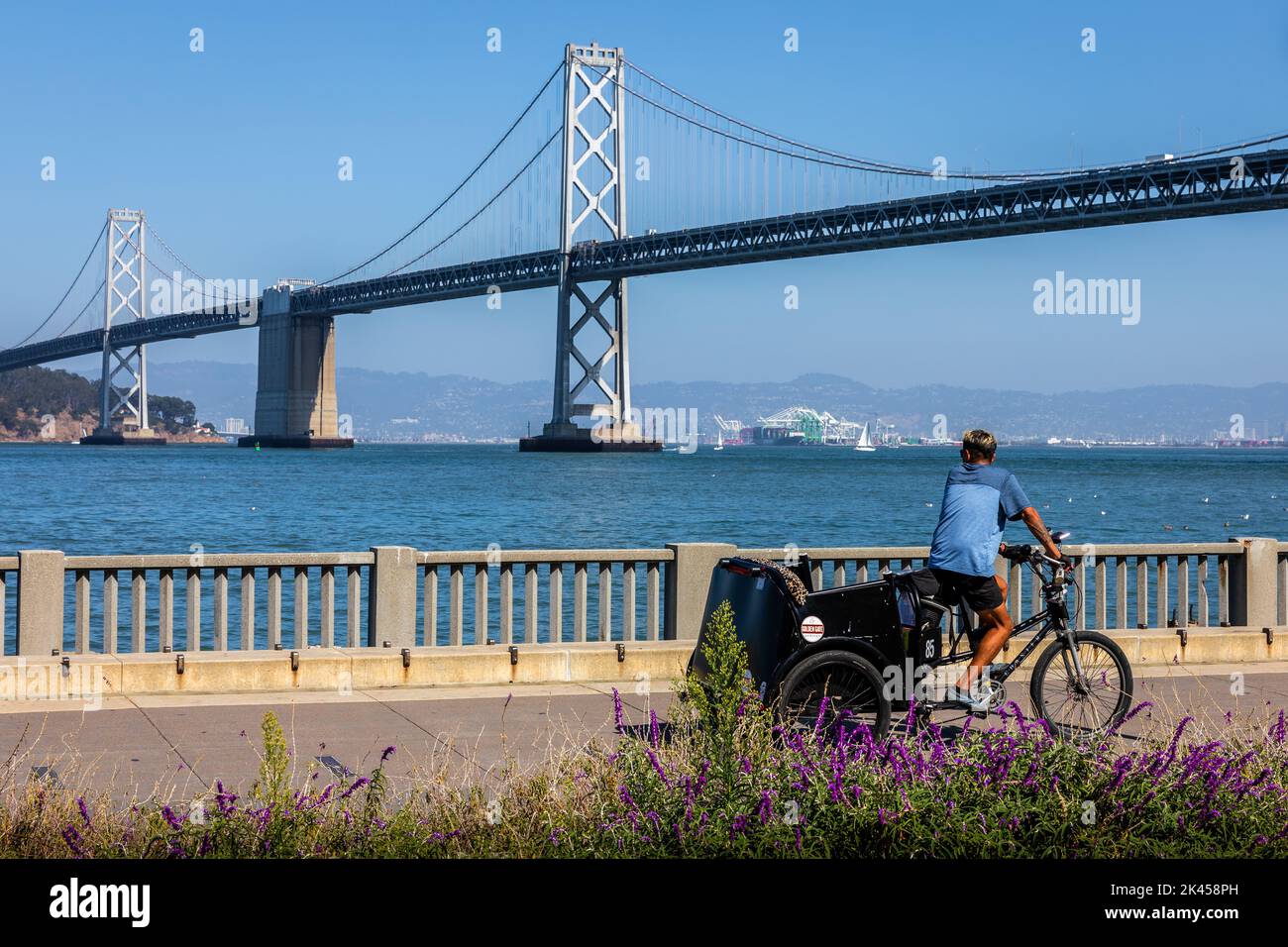 Californie, États-Unis - 27 septembre 2019: Blue shirt homme vélo trois roues avec substance sur le chemin de bord de mer avec fond de San Francisco - Oakl Banque D'Images