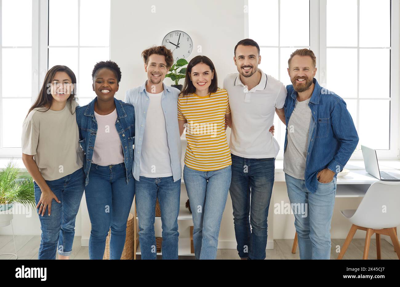 Heureux de divers amis de course mixte dans des vêtements décontractés cuddling ensemble regardant l'appareil photo et sourire. Banque D'Images