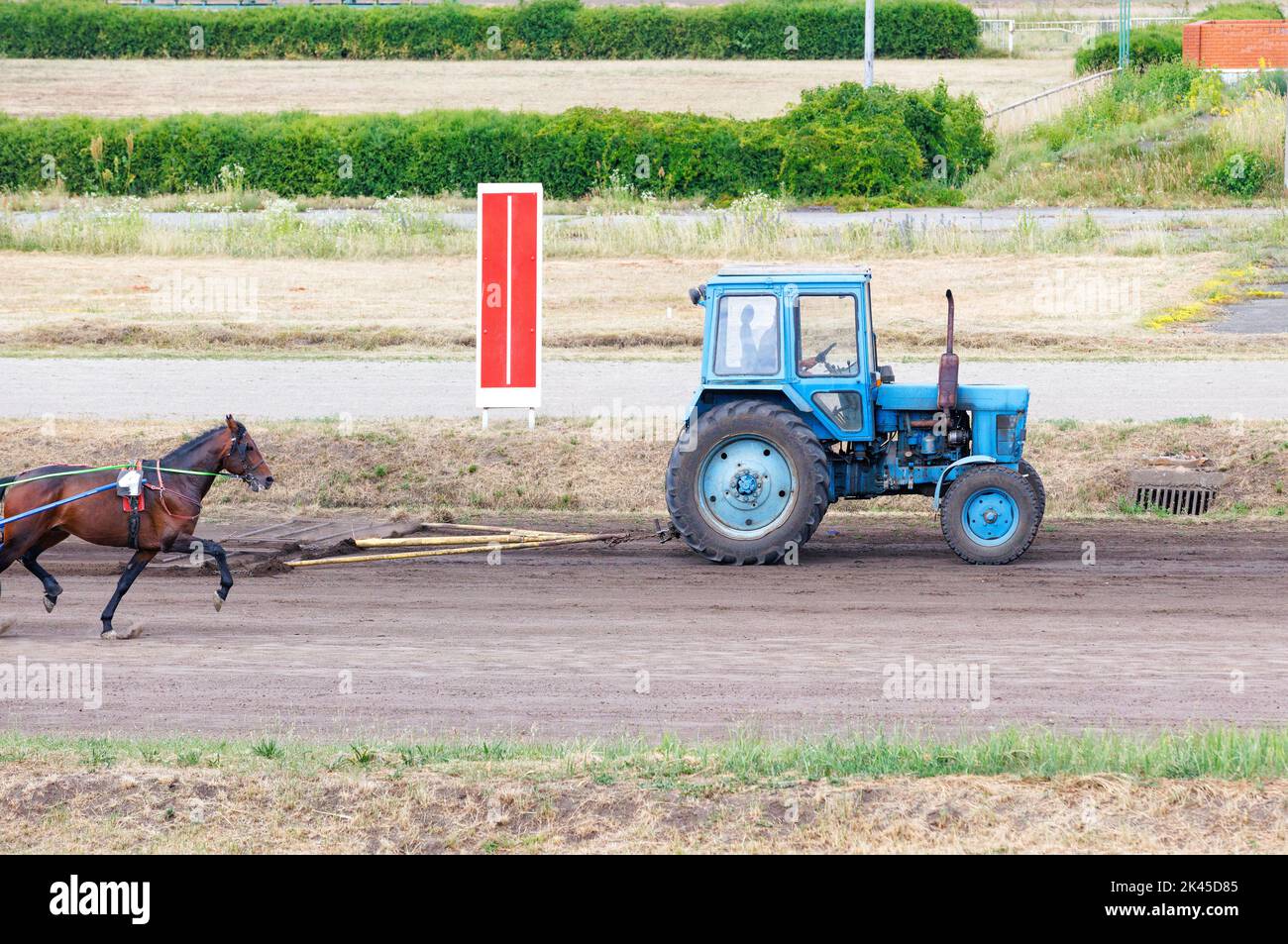 Un vieux tracteur prépare un itinéraire pour les chevaux sur l'hippodrome en le nivelant avec un attelage de remorquage. Copier l'espace. Banque D'Images