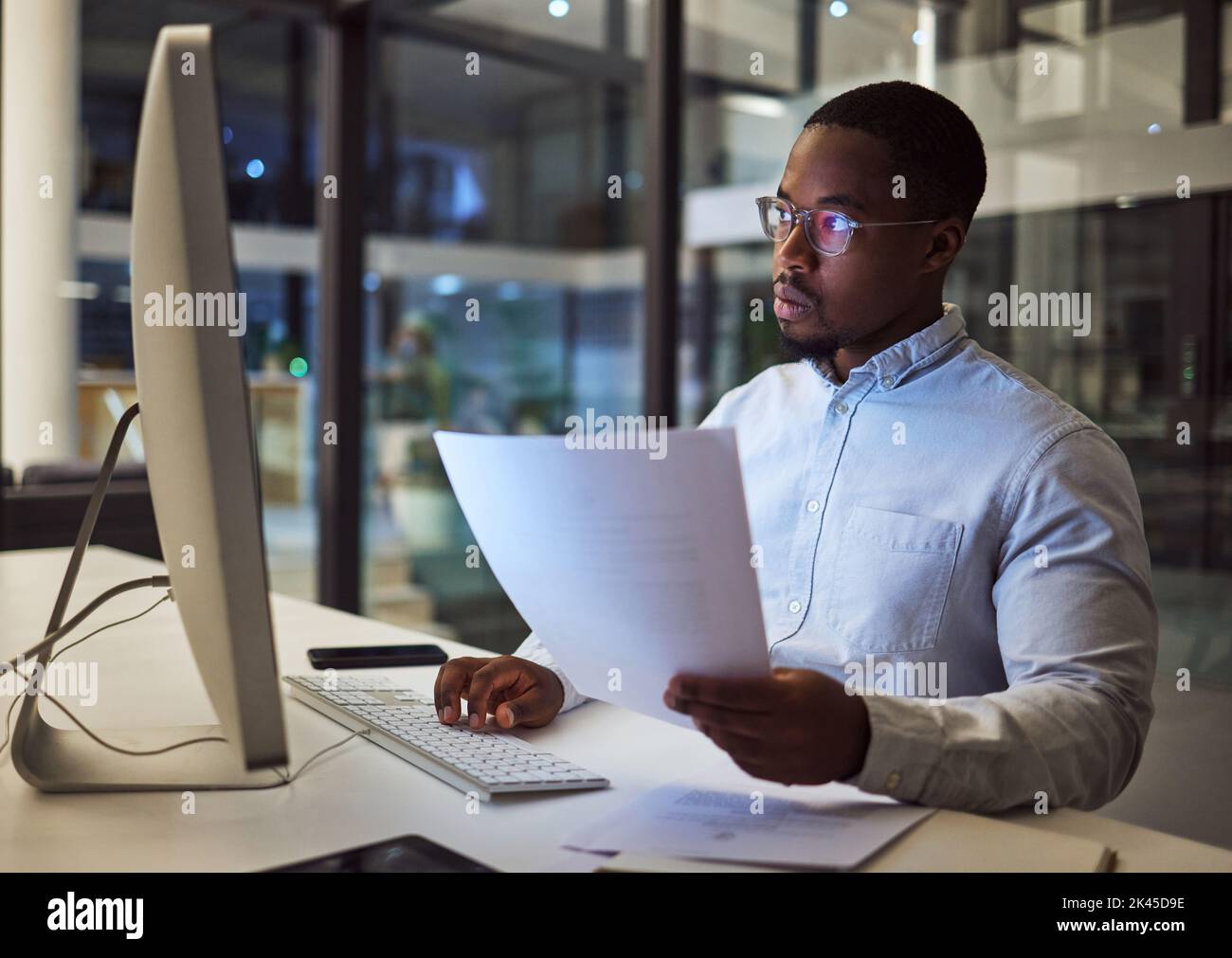 Contrat, documents et données avec un homme d'affaires travaillant la nuit sur un ordinateur dans un bureau. Recherche, lecture et information avec un homme noir Banque D'Images