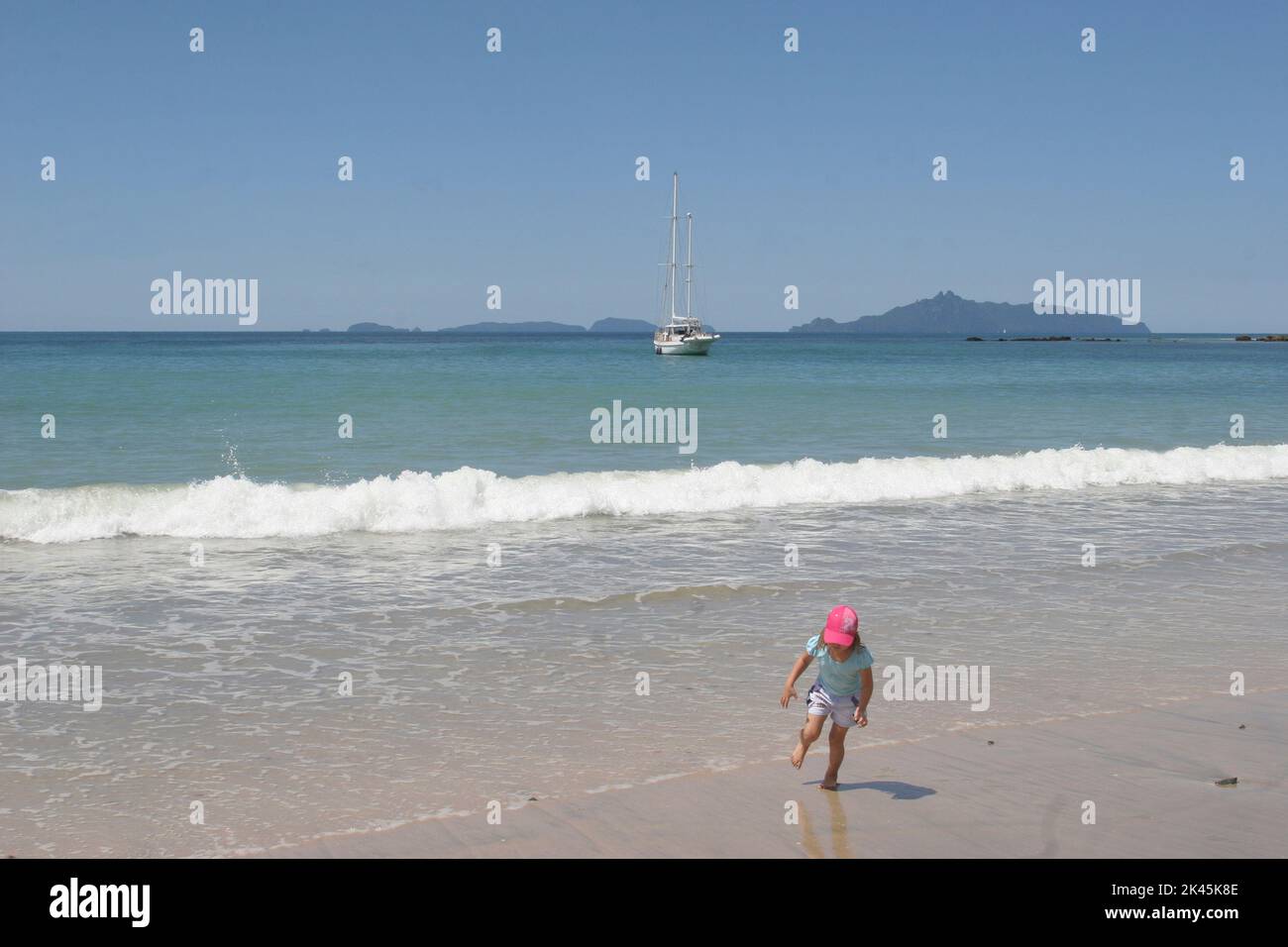 NEW ZEELAND un enfant joue sur l'une des plages de l'île du nord où un voilier est à l'ancre Banque D'Images
