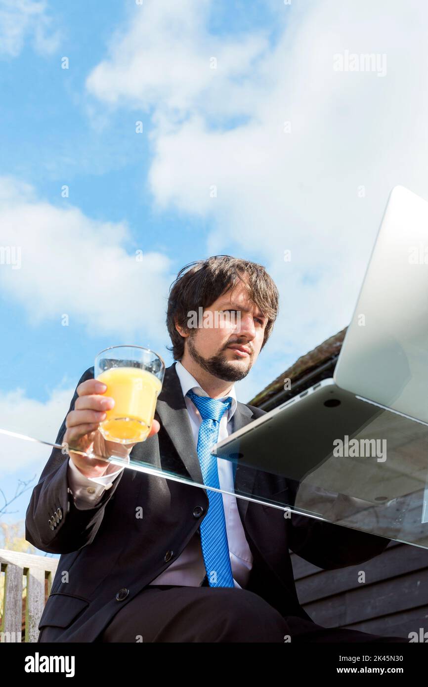 Homme tenant un verre de jus travaillant sur un bureau en verre à l'extérieur. Banque D'Images
