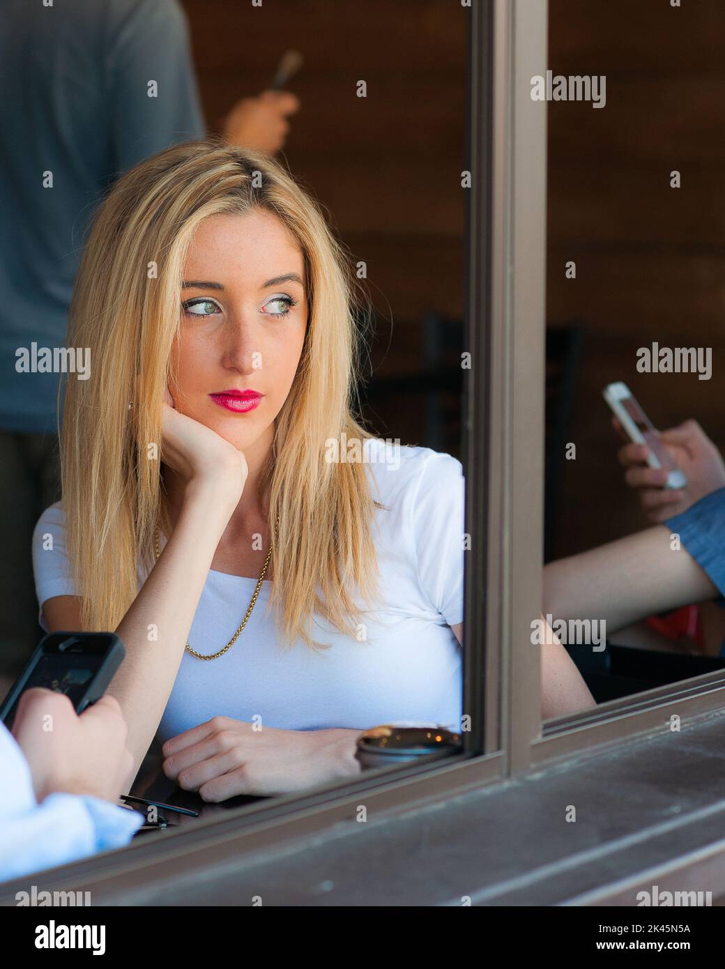Une femme qui regarde par la fenêtre du café tandis que d'autres personnes utilisent un smartphone. Banque D'Images