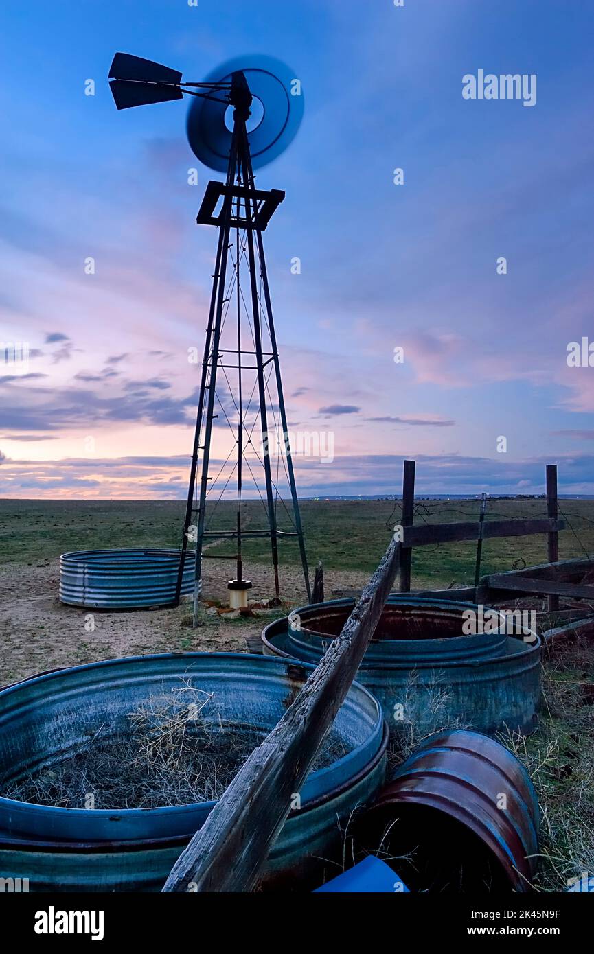 Un moulin à vent tournant roue métallique et tour de vent, mouvement flou, au coucher du soleil sur la prairie ou les hautes plaines du Colorado. Banque D'Images
