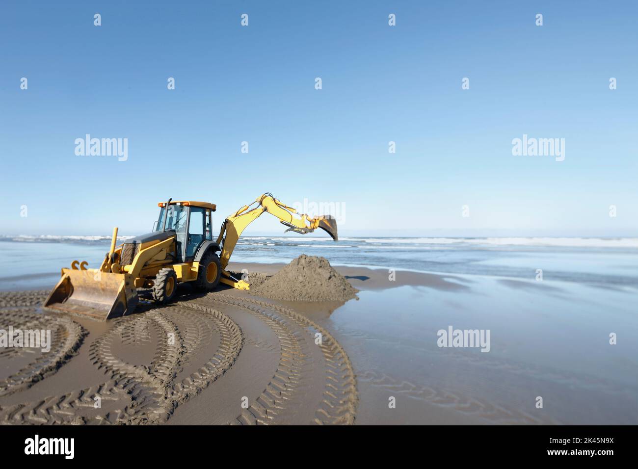 Une pelle rétro, creuseuse avec grande pelle travaillant sur le sable mou au bord de l'eau. Banque D'Images
