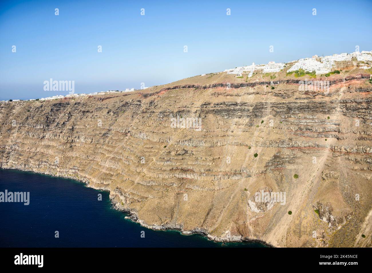 Les falaises et les formations rocheuses d'une île dans la mer Égée, avec une ville de maisons blanches au sommet des falaises. Banque D'Images