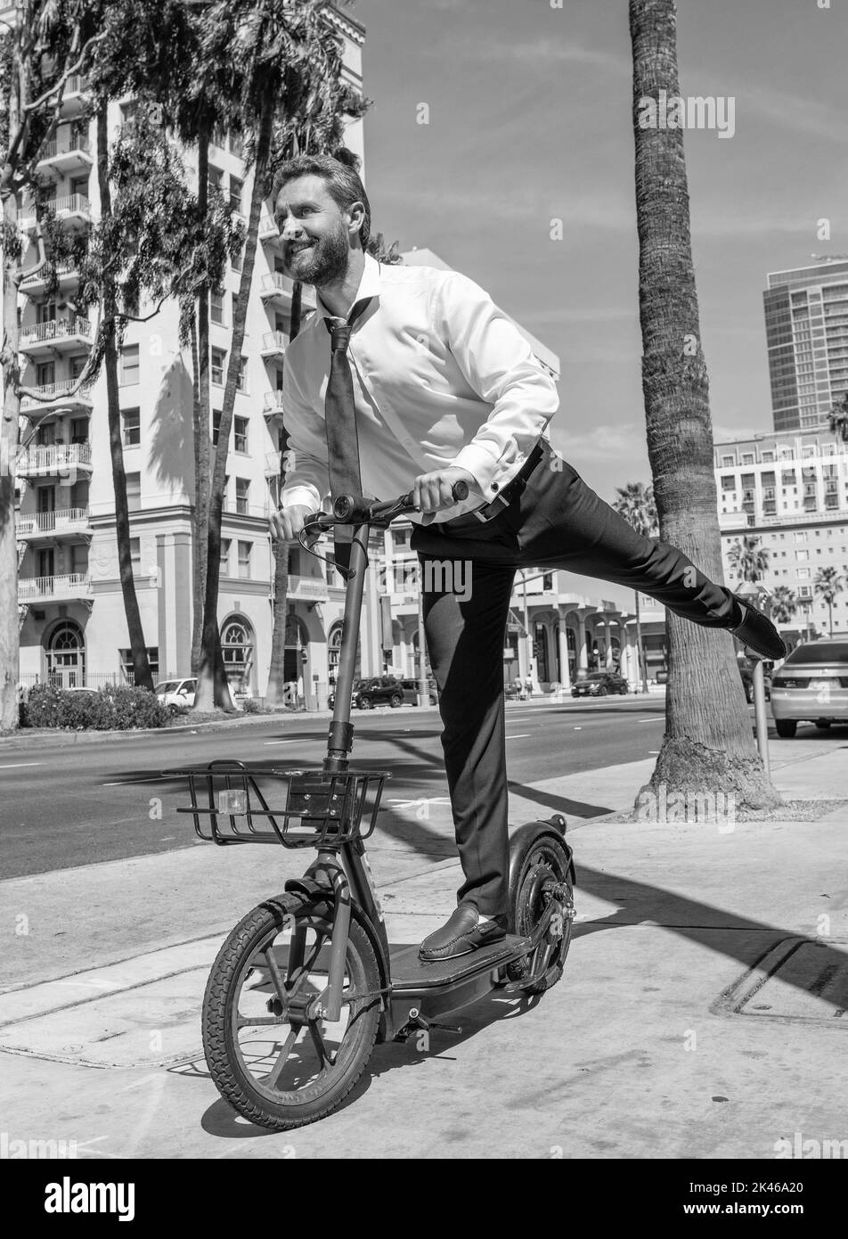 Un gars heureux en tenue de formalwear monter e-scooter le long du trottoir, actif Banque D'Images