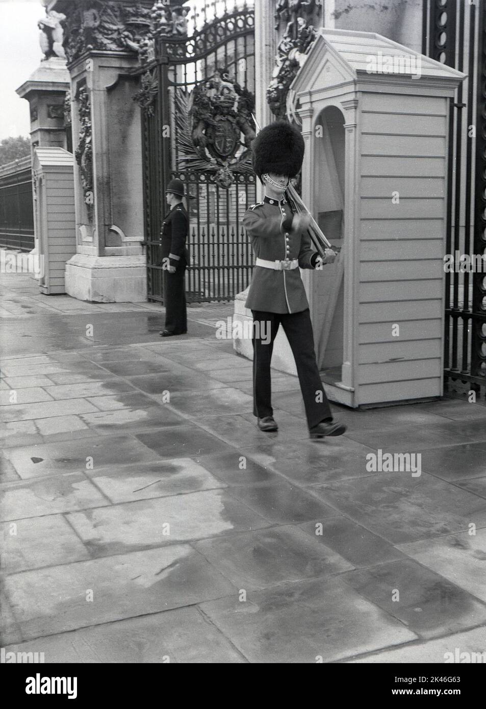 1958, historique, un policier et une garde de la Reine en uniforme en service à l'entrée devant Buckingham Palace, Westminster, Londres, Angleterre, Royaume-Uni. Guardsman dans leurs tuniques et peaux d'ours ont été en service de sentinelle devant Buckingham Palace, la résidence officielle de la reine, depuis que la reine Victoria a déménagé en 1837. Banque D'Images