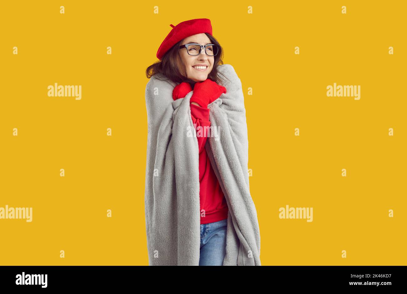 Femme en lunettes, gants rouges et chapeau enveloppés dans un tissu écossais, enroulé contre le froid sur fond jaune. Banque D'Images